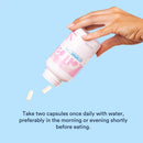 Hand holding a supplement bottle with capsules being poured, on a light blue background